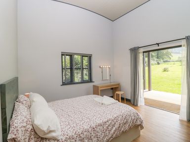 A bedroom with a bed a small desk a stool a window and an open door leading to a garden at Foxglove in Sticklinch West Pennard Glastonbury