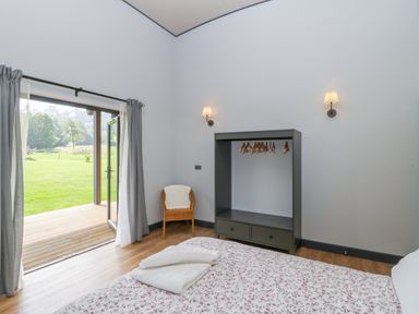 A bedroom with an open door to a garden a bed with floral bedding a wicker chair and a wardrobe with hangers at Foxglove in Sticklinch West Pennard Glastonbury