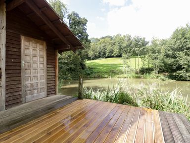 A wooden deck attached to a wooden cabin overlooking a pond and grassy hill at Foxglove in Sticklinch West Pennard Glastonbury