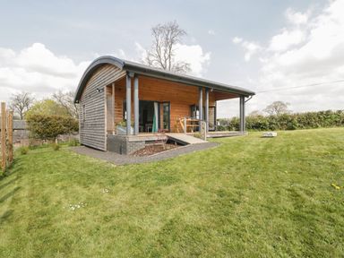 A small wooden cabin with a curved roof and porch on a grassy lawn at Foxglove in Sticklinch West Pennard Glastonbury
