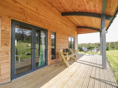 A wooden porch with a bench and two chairs with a small table on a grassy landscape at Foxglove in Sticklinch West Pennard Glastonbury