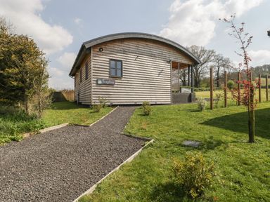 A wooden house with a curved roof and a gravel pathway surrounded by grass at Foxglove in Sticklinch West Pennard Glastonbury