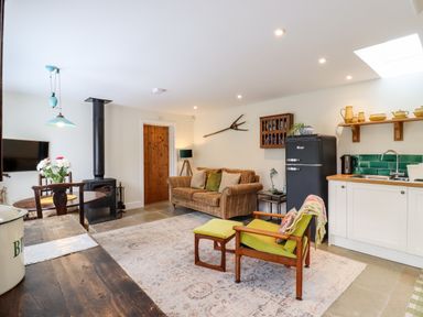 A living room with a sofa an armchair a wood stove a dining table and an open kitchen at Courtyard Cottage Poplar Farm Barn in Sweffling near Saxmundham