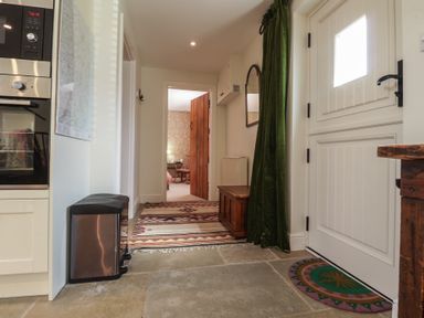 A hallway with stone floor a white door a green curtain a wooden chest and a view into a room with floral wallpaper at Courtyard Cottage Poplar Farm Barn Sweffling near Saxmundham