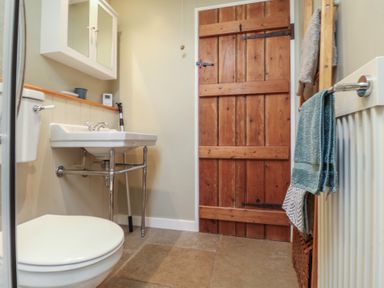 A bathroom with a toilet sink wooden door and towels at Courtyard Cottage Poplar Farm Barn Sweffling near Saxmundham