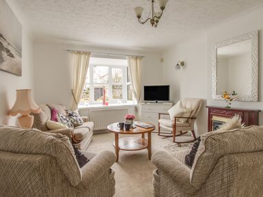A living room with beige sofas armchairs a wooden coffee table television and window at Casa Carmen Weymouth