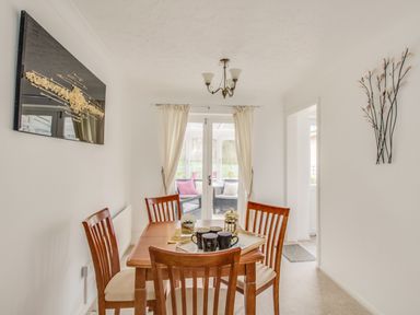 A dining room with wooden table and chairs and glass doors leading to a sitting area at Casa Carmen in Weymouth