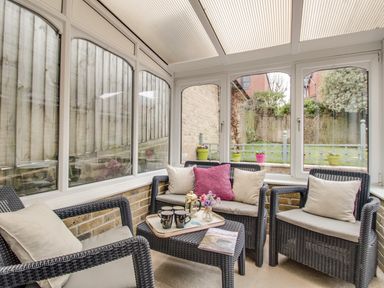 A conservatory with wicker chairs and a table holding a tray with mugs and a flower vase at Casa Carmen in Weymouth