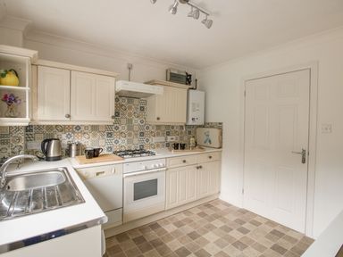 A kitchen with white cabinets a dishwasher a sink a stovetop oven and patterned tile backsplash at Casa Carmen in Weymouth