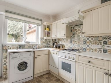 A kitchen with patterned tile backsplash washing machine oven and cream cabinets at Casa Carmen in Weymouth