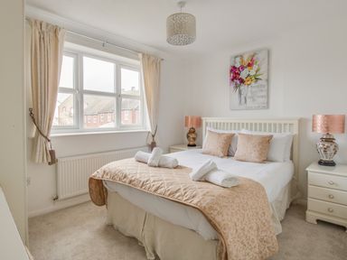 A bedroom with a double bed with pillows and towels bedside tables with lamps and a window with curtains at Casa Carmen in Weymouth
