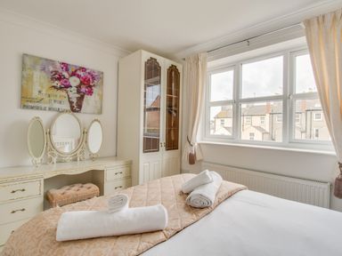 A bedroom with a bed and rolled towels a dressing table with a mirror and a wardrobe beside a window at Casa Carmen Weymouth