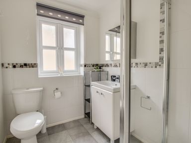 A bathroom with a toilet a sink with cabinet a shelving unit a window and a shower at Casa Carmen in Weymouth