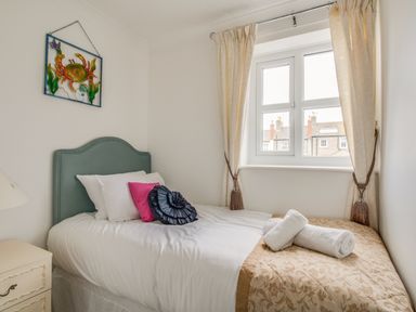 A bedroom with a single bed white bedding decorative pillows and rolled towels by the window at Casa Carmen in Weymouth