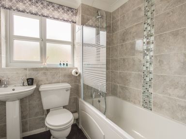A bathroom with a toilet sink bathtub and window with patterned blind at Casa Carmen in Weymouth