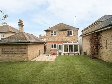 A backyard with a lawn and a brick house with a conservatory and adjacent outbuildings at Casa Carmen Weymouth
