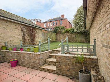 An outdoor patio area with tiled floor stairs leading to a grassy yard with small fences and flower pots at Casa Carmen in Weymouth