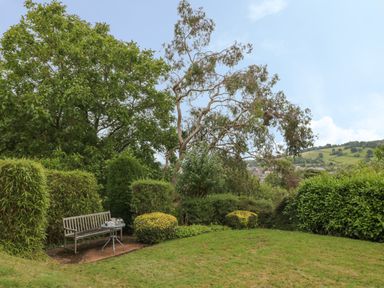 A garden with a wooden bench and round metal table surrounded by bushes and trees at The Old Vicarage in Tiverton