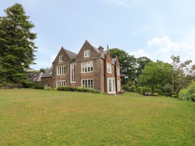 A stone house with multiple windows surrounded by trees and grass at The Old Vicarage in Tiverton