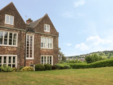 The exterior of a brick house with multiple windows and a lawn with shrubs and hedges at The Old Vicarage in Tiverton