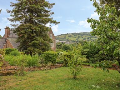 A garden with trees shrubs and a house in the background at The Old Vicarage in Tiverton