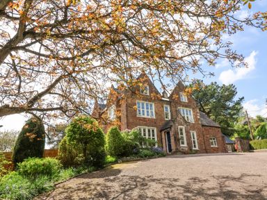 A stone house with multiple windows and a driveway surrounded by trees and shrubs at The Old Vicarage in Tiverton