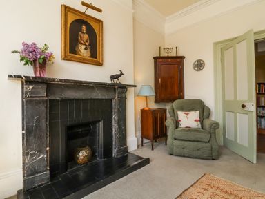 A living room with a black marble fireplace chair with floral cushion and wooden cabinets at The Old Vicarage in Tiverton