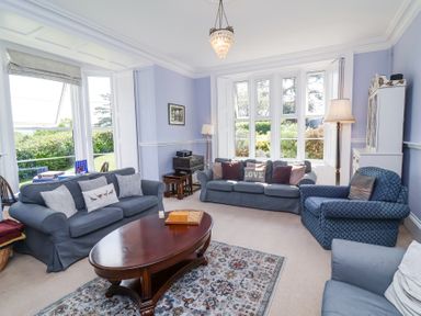 A living room with blue sofas a wooden coffee table a patterned rug and large windows at The Old Vicarage in Tiverton