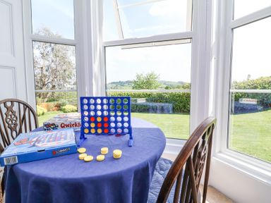 A table with a blue tablecloth and a Connect 4 game with yellow and red pieces next to a window with outdoor view at The Old Vicarage in Tiverton