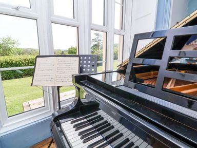 A grand piano with sheet music on a stand by a window overlooking a garden at The Old Vicarage in Tiverton