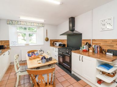 A kitchen with a wooden table and chairs a black stove microwave and wooden countertops at The Old Vicarage in Tiverton