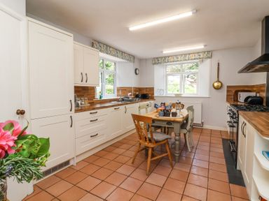 A kitchen with a wooden table and chairs in the center and windows on two walls at The Old Vicarage in Tiverton