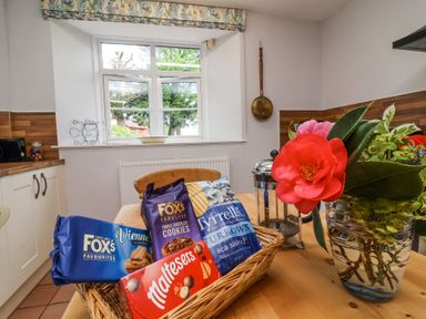 A kitchen table with a basket of snacks and a vase of flowers near a window at The Old Vicarage in Tiverton