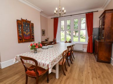 A dining room with a long table and red chairs under a chandelier at The Old Vicarage in Tiverton