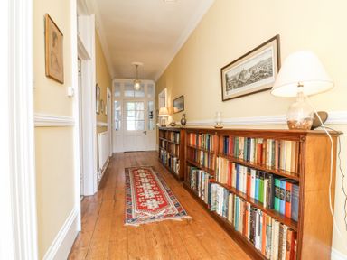 A hallway with wooden floor a red patterned rug bookshelves along the right wall and framed pictures at The Old Vicarage in Tiverton