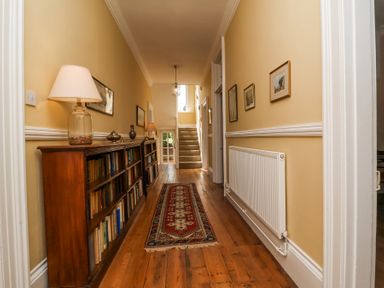 A hallway with wooden floor a bookshelf a rug and stairs at The Old Vicarage in Tiverton