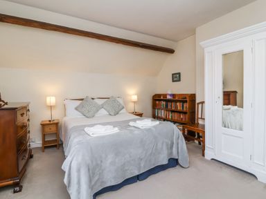 A bedroom with a bed, bedside tables with lamps, a chest of drawers, a bookshelf, a bench, and a mirrored wardrobe at The Old Vicarage in Tiverton