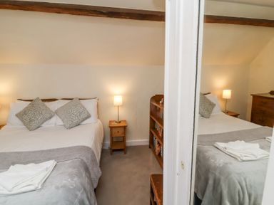 A bedroom with a double bed two patterned pillows bedside table with lamp and a wooden chest of drawers at The Old Vicarage in Tiverton