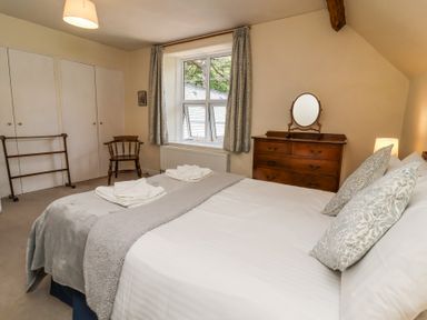 A bedroom with a bed pillows dresser chair and window at The Old Vicarage in Tiverton