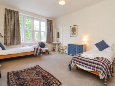 A bedroom with two single beds a blue dresser a chair and a window with curtains at The Old Vicarage in Tiverton