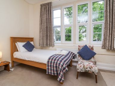 A bedroom with a wooden bed a floral chair and multiple windows at The Old Vicarage in Tiverton