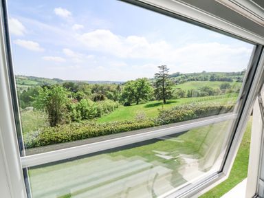 A view of green fields and trees through an open window at The Old Vicarage in Tiverton
