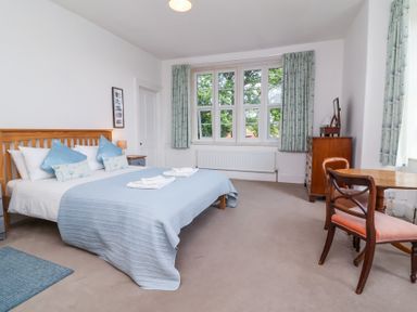 A bedroom with a double bed blue bedding wooden furniture and large window at The Old Vicarage in Tiverton