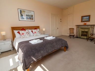 A bedroom with a wooden bed with pillows and folded towels bedside tables with lamps a fireplace and two wooden chairs at The Old Vicarage in Tiverton