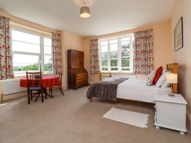 A bedroom with a bed bedside table and lamp a round table with chairs and curtains on windows at The Old Vicarage in Tiverton