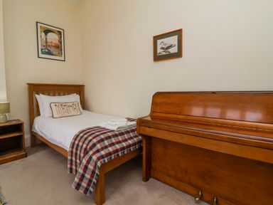A bedroom with a single bed a plaid blanket wooden piano and framed pictures on the wall at The Old Vicarage in Tiverton