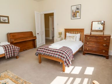 A bedroom with two single beds a piano a wooden dresser with mirror and a nightstand with lamp at The Old Vicarage in Tiverton