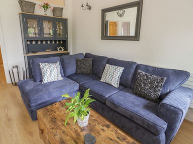 A living room with a blue sectional sofa with cushions a wooden coffee table with a plant and a cabinet with glass doors at The Barn in Droitwich Spa