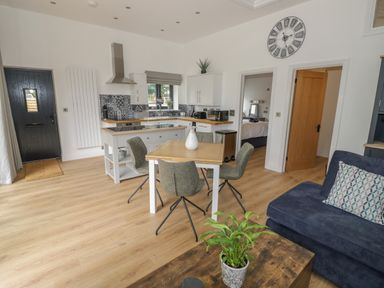 A kitchen and dining area with a wooden table and chairs a blue sofa and a wooden coffee table with a plant at The Barn in Droitwich Spa