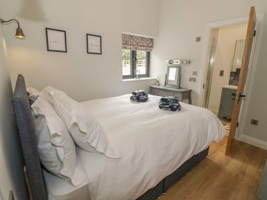 A bedroom with a bed white bedding and a dresser near a window at The Barn in Droitwich Spa